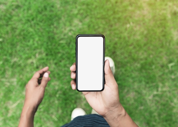 Foto hombre que sostiene el teléfono que muestra la pantalla en blanco caminando sobre el césped