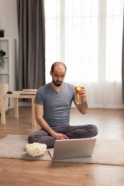 Hombre que sostiene el vaso de cerveza mientras habla con amigos en la computadora portátil.