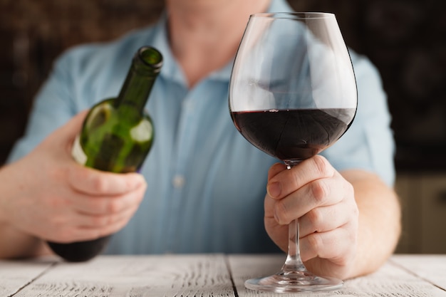 hombre que sostiene un vaso con vino tinto y una botella