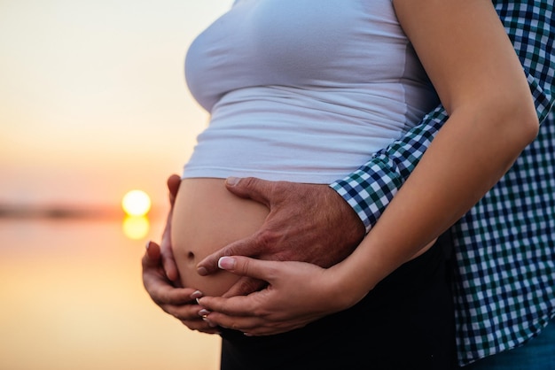 Hombre que sostiene el vientre embarazado de la mujer al aire libre en una puesta de sol