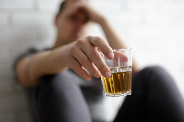 Hombre que sufre de alcoholismo cerca del vaso de whisky en la mano masculina