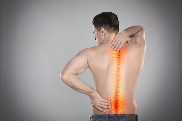 Hombre que sufre de dolor en la columna vertebral sobre fondo gris