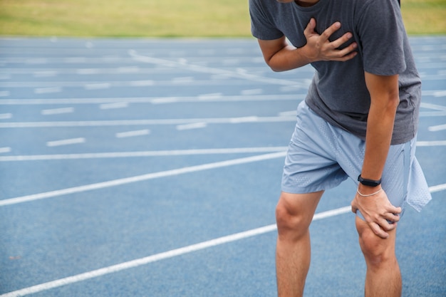 Hombre que sufre de dolor en el pecho o síntomas de enfermedad cardíaca mientras se ejecuta en la pista de goma azul.