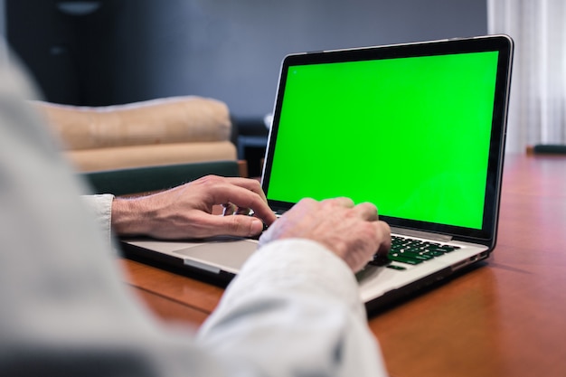 Hombre que trabaja en casa en una computadora con pantalla verde.