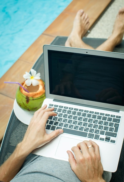 Un hombre que trabaja en la computadora al lado de la piscina.