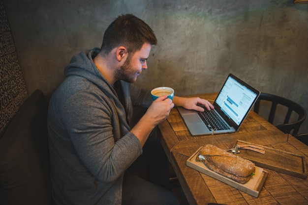 Hombre que trabaja en la computadora portátil en café sándwich de desayuno y café