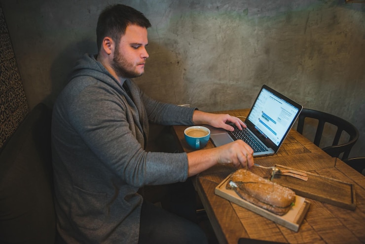Foto hombre que trabaja en la computadora portátil en café sándwich de desayuno y café
