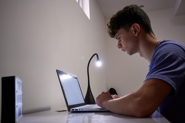 Un hombre que trabaja en la computadora portátil con una lámpara y un escritorio.