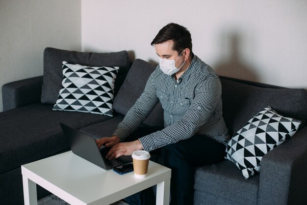 Hombre que trabaja en la computadora portátil con máscara de oficina en casa