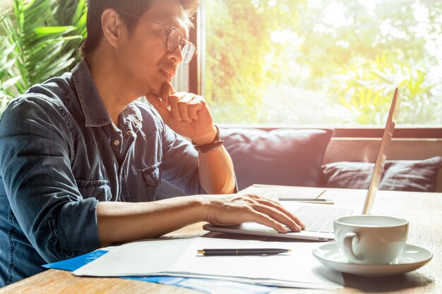 Hombre que trabaja en la computadora portátil con el papel del documento y la taza de café en el escritorio de madera