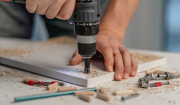 Hombre que trabaja con un destornillador eléctrico durante el proceso de fabricación de muebles de madera en el taller