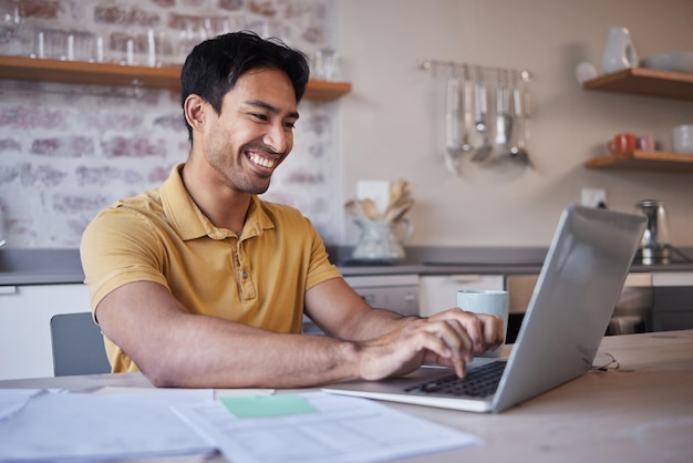 Hombre que trabaja en un informe desde casa o usa una computadora portátil para buscar en Internet en la mesa de su cocina Asiático con una sonrisa feliz escribiendo en línea y en comunicación en el correo electrónico de las redes sociales o trabajo independiente