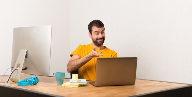 Hombre que trabaja con laptot en una oficina extendiendo las manos hacia un lado para invitar a venir