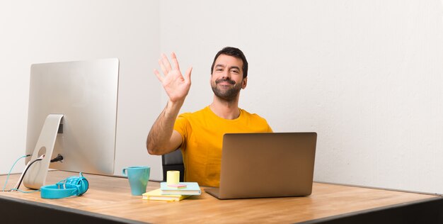 Hombre que trabaja con laptot en una oficina saludando con la mano con expresión feliz