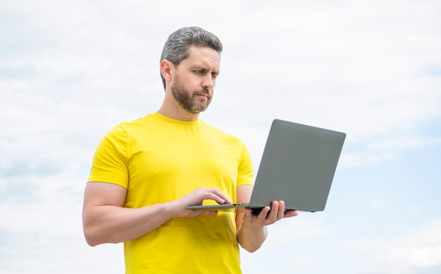 Hombre que trabaja en línea en la computadora portátil en el fondo del cielo