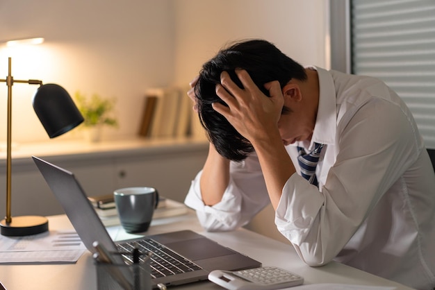 hombre que trabaja en la oficina esta noche sosteniendo su cabeza por estar estresado por el trabajo