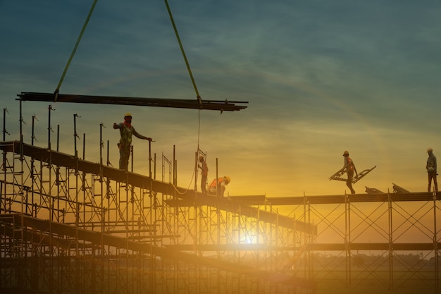 Hombre que trabaja en el sitio de construcción con andamios y edificio con fondo de puesta de sol, andamios para fábrica de construcción