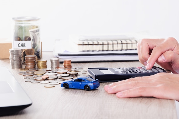 Hombre que usa la calculadora con el juguete del coche y pila de moneda para el préstamo de seguro o Ahorro para la compra de concepto de coche