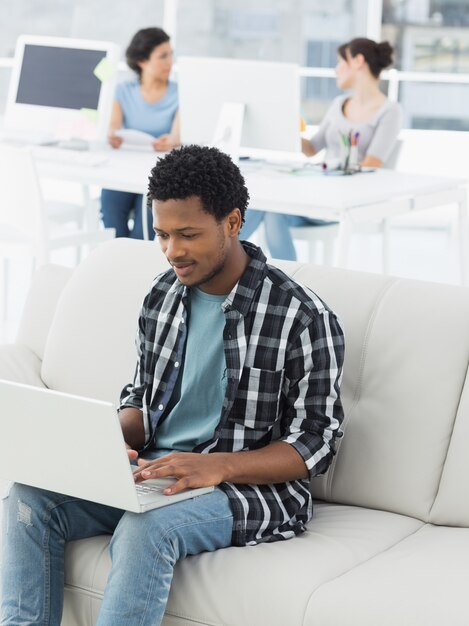 Hombre que usa la computadora portátil con los colegas en la oficina creativa