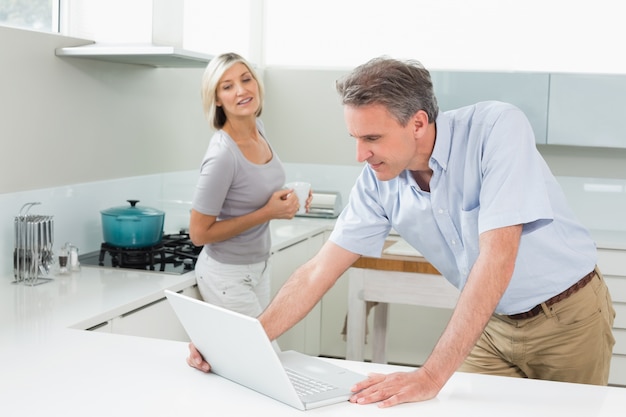 Hombre que usa la computadora portátil mientras que mujer en la cocina