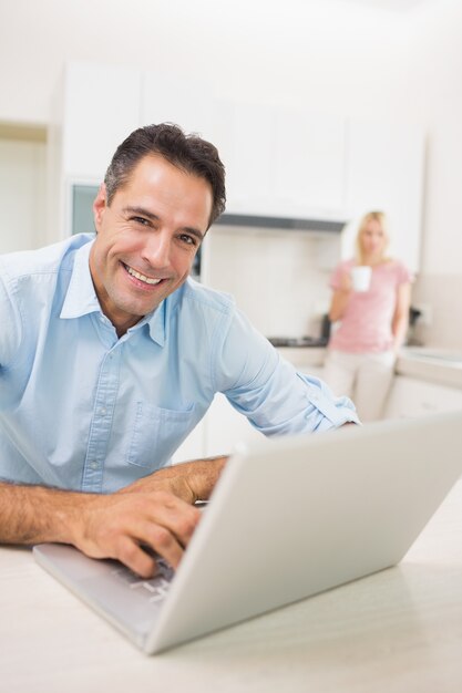 Hombre que usa la computadora portátil con la mujer que bebe el café en la cocina