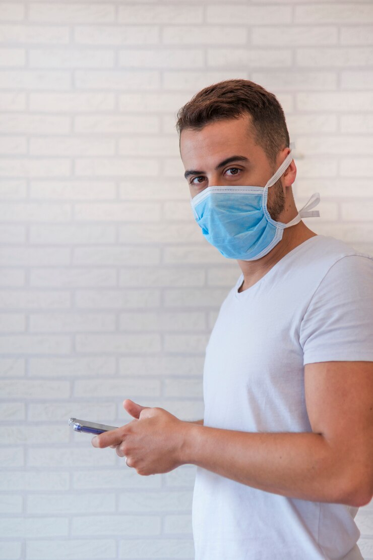 Hombre que usa una máscara de protección antivirus para evitar que otros contraigan coronavirus COVID-19 y SARS cov 2, mientras se comunica con sus seres queridos con su teléfono inteligente desde su casa.