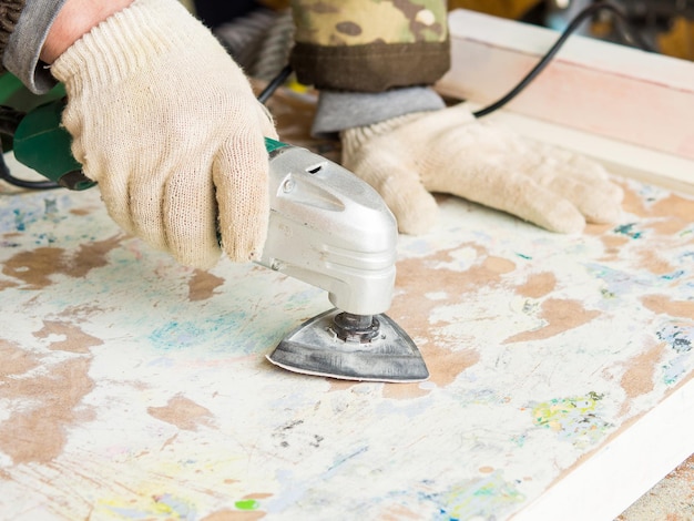 Un hombre que usa un molinillo quita la pintura vieja de la restauración de muebles del concepto hecho a mano de muebles antiguos