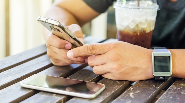 Hombre que usa un smartphone y un smartwatch en una cafetería.