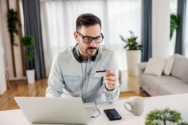 Un hombre que usa tarjeta de crédito para comprar en línea en la computadora portátil en su acogedor hogar