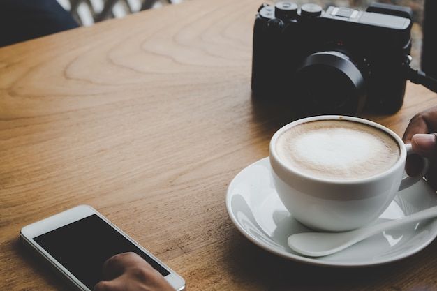 hombre que usa el teléfono con café y cámara en la mesa de madera