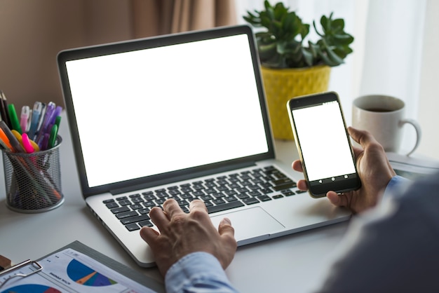 Hombre que usa el teléfono inteligente y la computadora portátil en la oficina