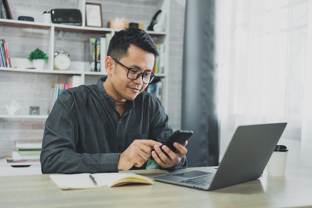 Hombre que usa un teléfono inteligente después de trabajar con una computadora portátil en la mesa hombre de negocios que usa un teléfono móvil para buscar en las redes sociales o comprar en línea o en acciones o criptomonedas Conferencia de conversación de teléfonos inteligentes