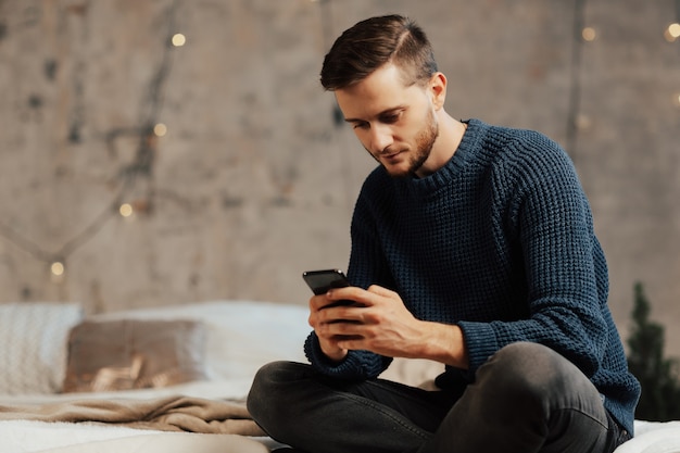 Hombre que usa el teléfono móvil mientras está sentado en la cama.