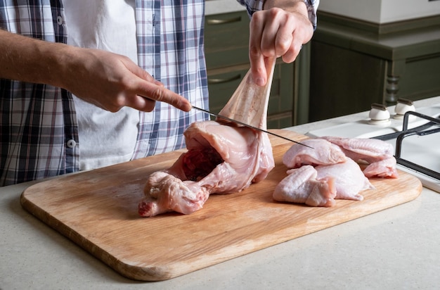 El hombre quita la piel de la pechuga de pollo cruda Cortando el pollo en trozos