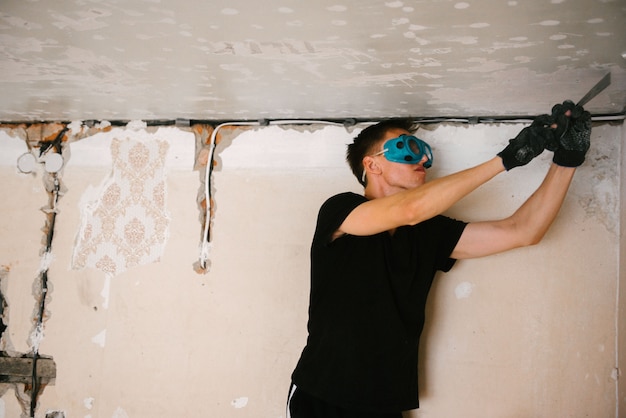 Un hombre quita pintura vieja del techo con una espátula