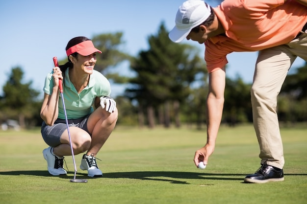 Hombre quitando la pelota de golf del hoyo por una mujer sonriente