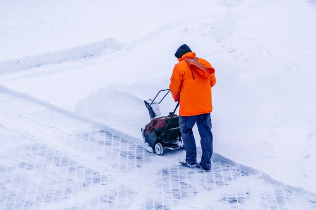 Hombre con quitanieves de accionamiento de vía motorizada borra la nieve, un quitanieves en un detalle de carretera nevada. Máquina motorizada para quitar nieve pesada y húmeda. Equipo lanzador de nieve.