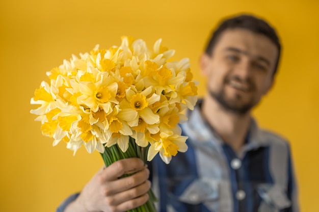 Un hombre con un ramo de flores en una pared de color.