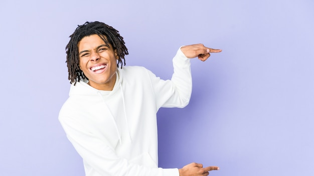 Hombre rasta afroamericano joven emocionado señalando con los dedos índices de distancia.