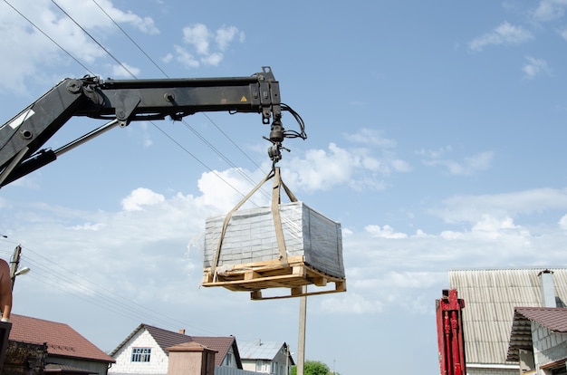 Un hombre de raza europea ayuda a cargar baldosas al suelo desde un coche. Entrega y descarga de materiales de construcción a la vivienda. Camión grúa descargado baldosas de la calle.