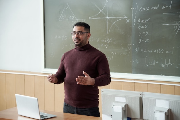 Hombre de raza mixta explicando algo a los estudiantes por pizarra