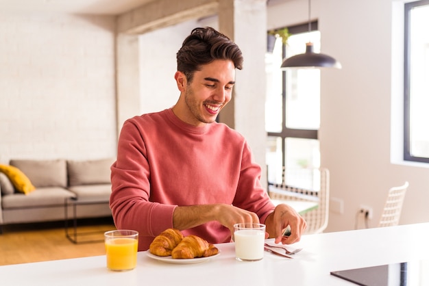 Foto hombre de raza mixta joven comiendo croissant en una cocina en la mañana