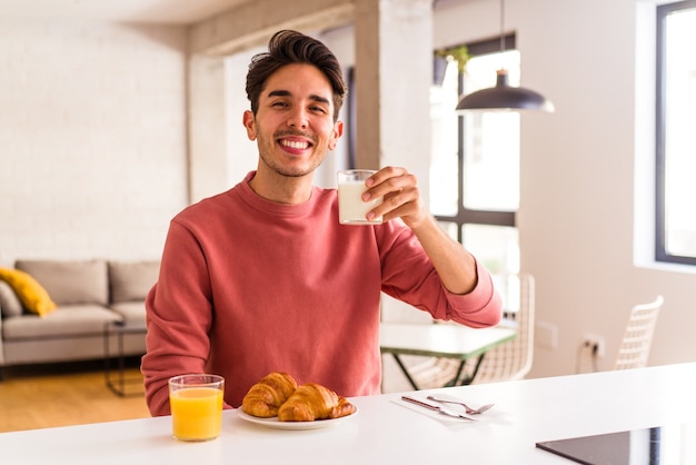 Foto hombre de raza mixta joven comiendo croissant en una cocina en la mañana