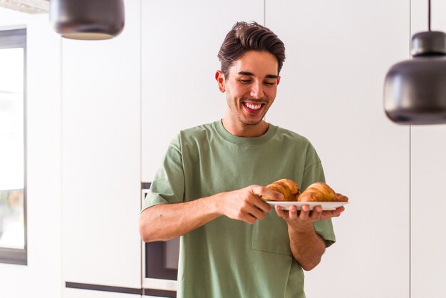 Hombre de raza mixta joven comiendo croissant en una cocina en la mañana