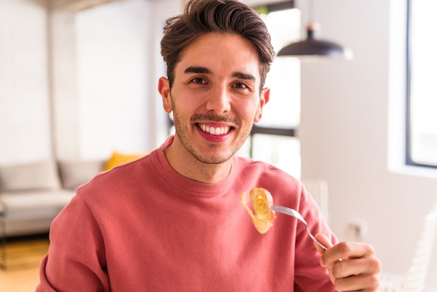 Hombre de raza mixta joven comiendo croissant en una cocina en la mañana