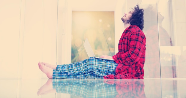 Hombre real usando una computadora portátil en el piso en casa disfrutando de relajarse