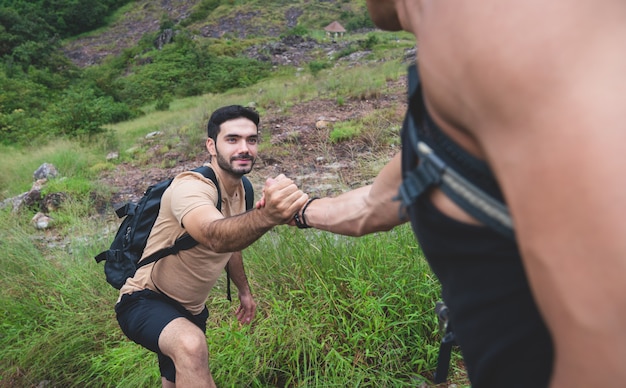 Hombre recibiendo ayuda de su amigo mientras camina en las montañas