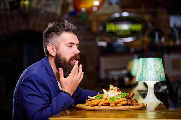 El hombre recibió comida con carne de papas fritas, palitos de pescado. Se merece una comida deliciosa. Disfrute de su comida. Merienda alta en calorías. Comida deliciosa. Relájate después de un duro día. Traje formal de hombre de negocios sentarse en el restaurante.