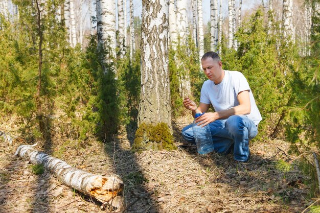 El hombre recoge la savia de abedul en el bosque de la primavera