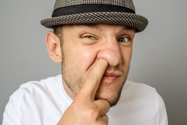 Hombre recogiendo su nariz sobre fondo gris